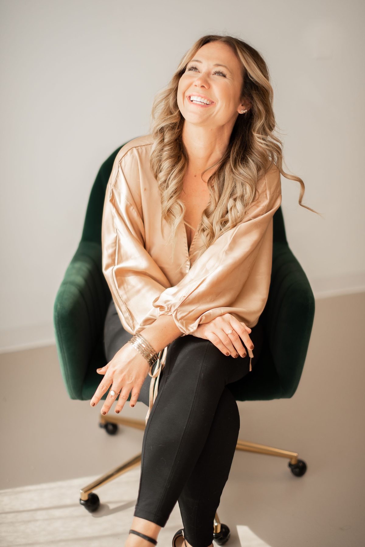 Ashley Diaz Bravo, founder of Ashley R Marketing, laughing in a gold blouse on a green velvet chair